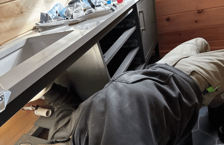 Person working under a kitchen sink repairing plumbing.